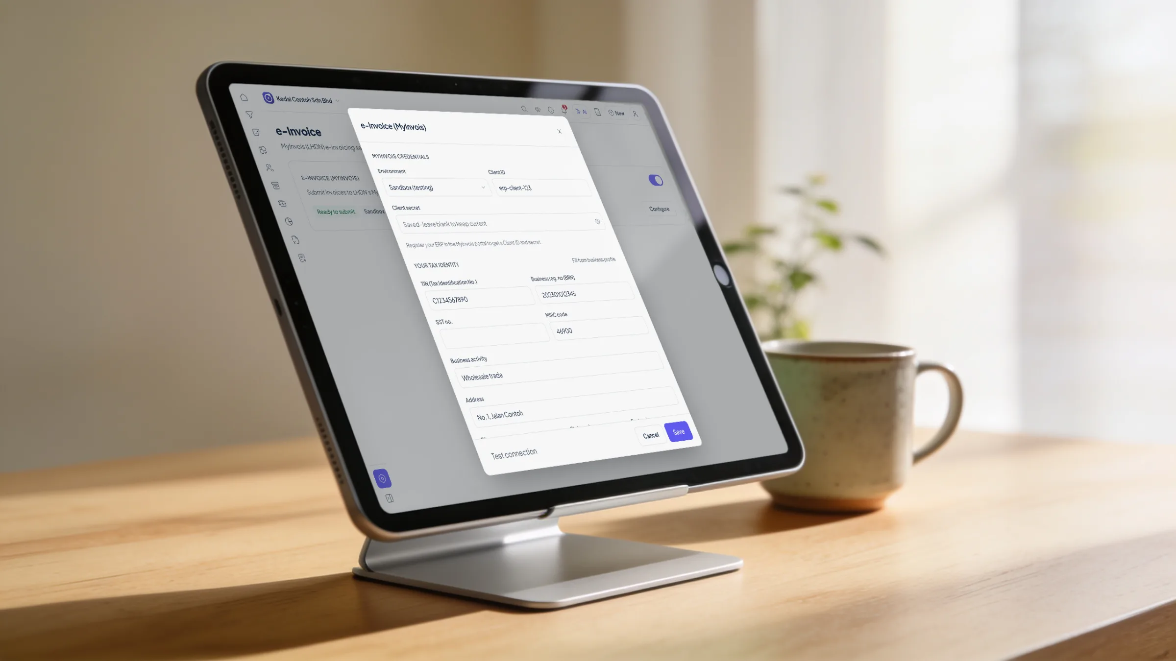 A tablet on a stand on an oak desk showing the Orbit Finance e-Invoice (MyInvois) setup: environment, client ID, TIN, business registration number and MSIC code
