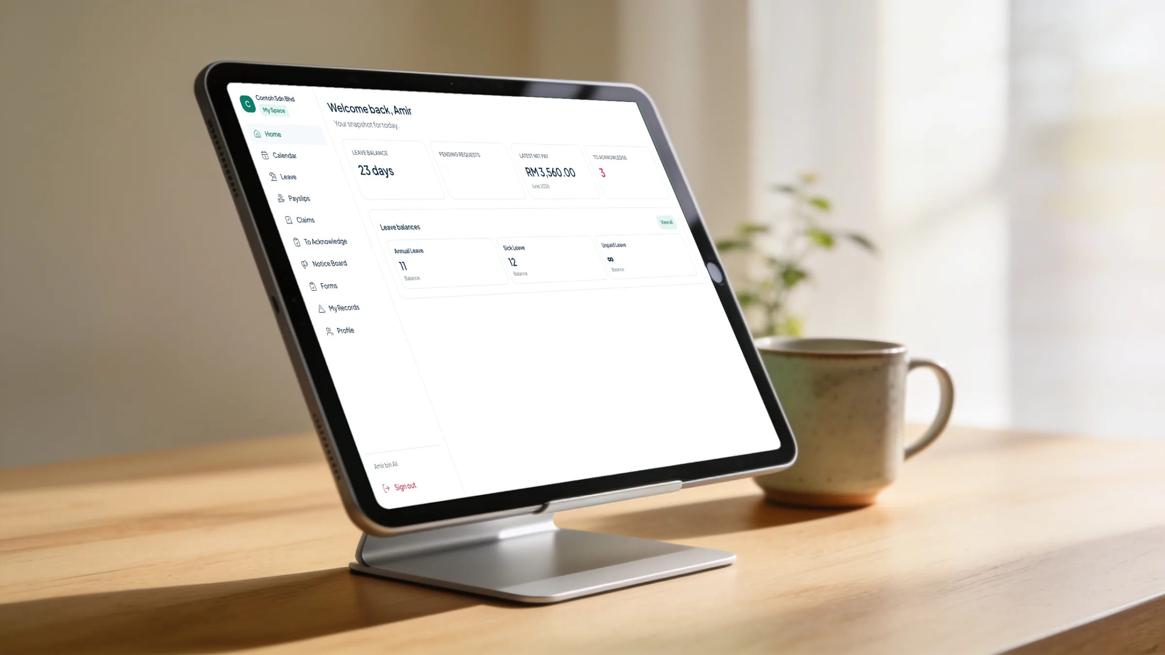 A tablet on a desk stand beside a coffee mug, showing Orbit HR employee self-service: Amir's leave balance of 23 days, his latest net pay of RM 3,560.00 and three items to acknowledge