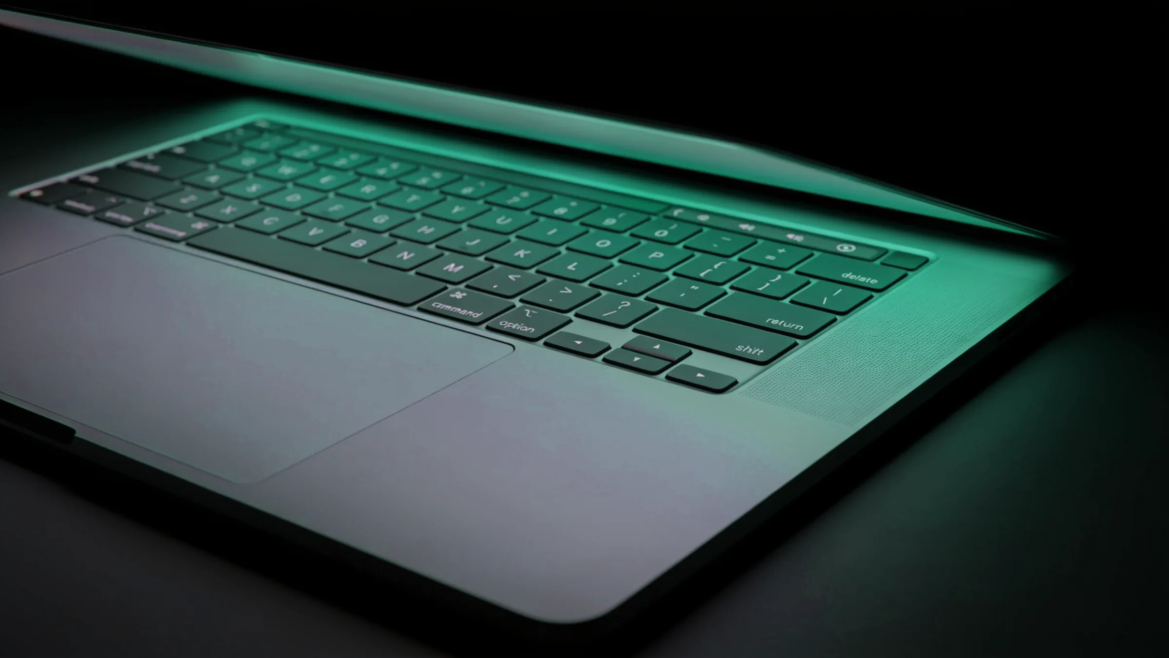 Close-up of a laptop keyboard edge lit by a soft teal glow in a dark room