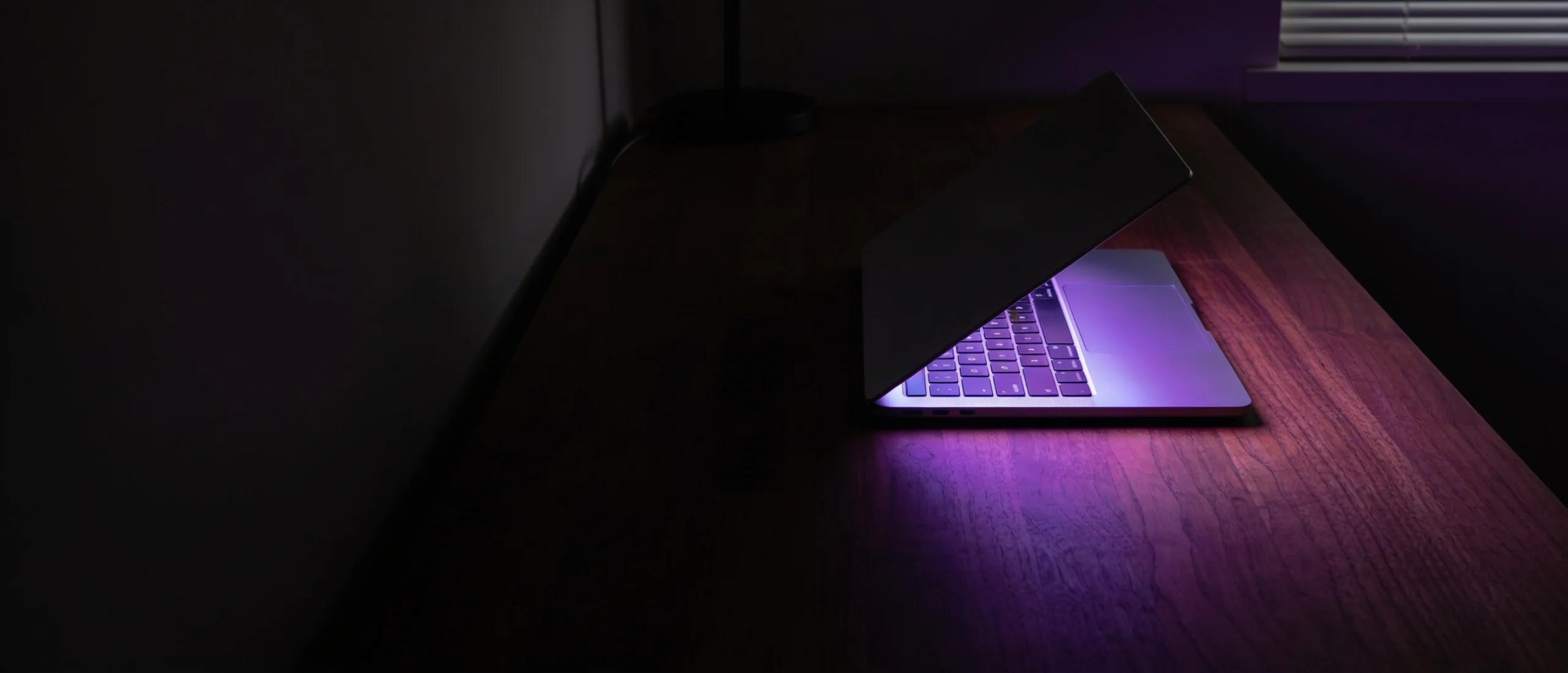 A laptop glowing indigo on a desk in a dark room at night