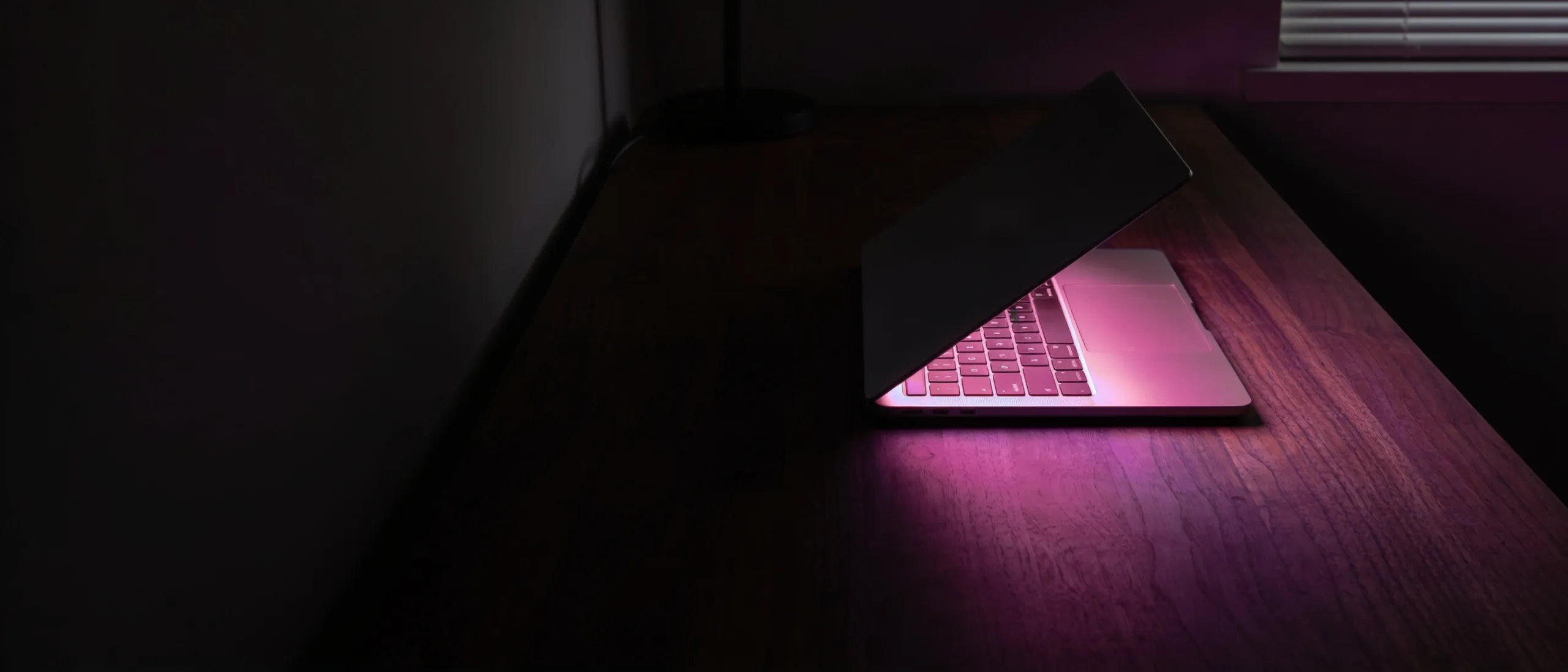 A laptop glowing berry on a desk in a dark room at night