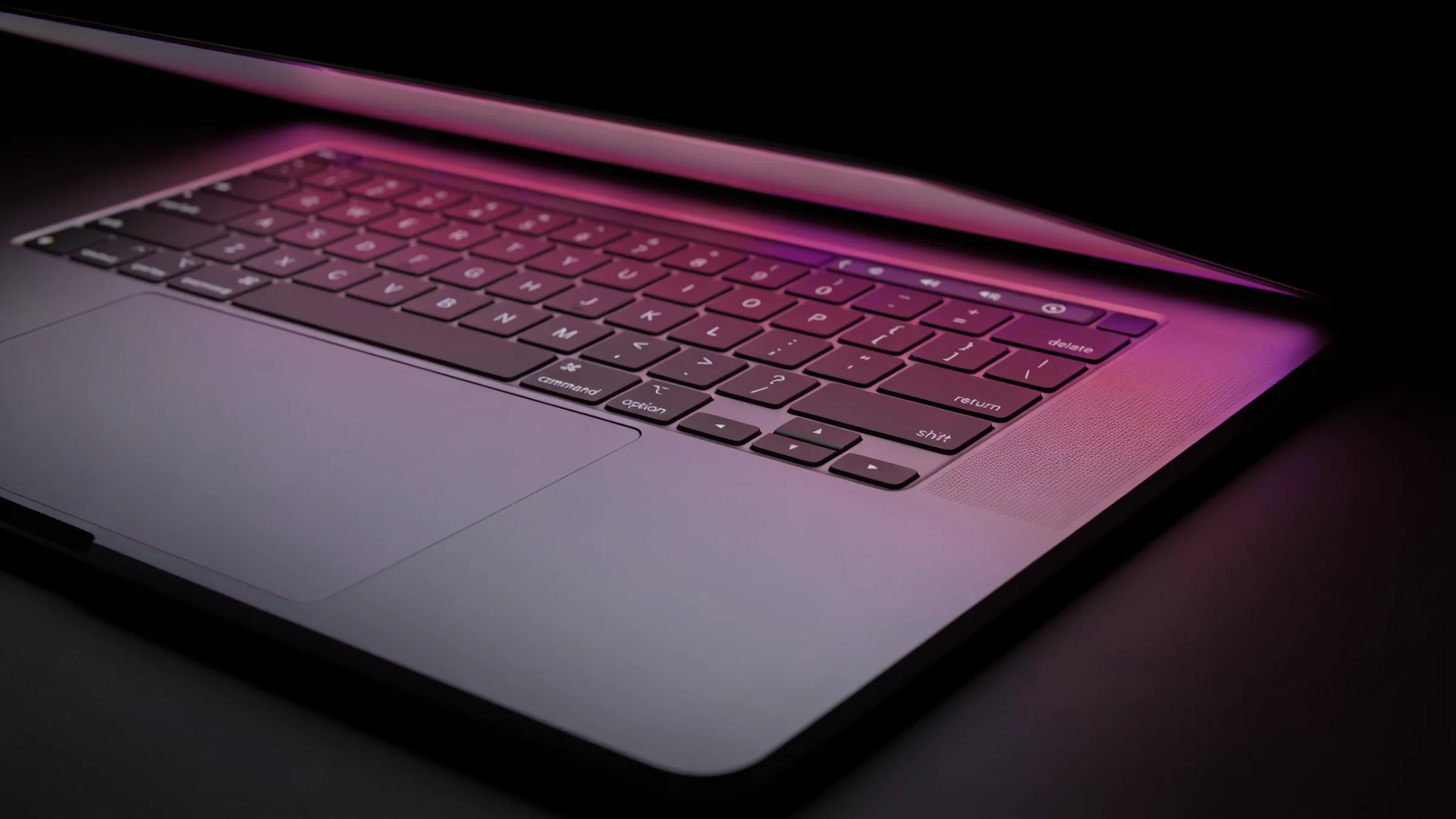 Close-up of a laptop keyboard edge lit by a soft berry glow in a dark room